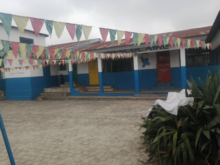 Cour de l'école décorée de fanions colorés, devant un bâtiment bleu et blanc