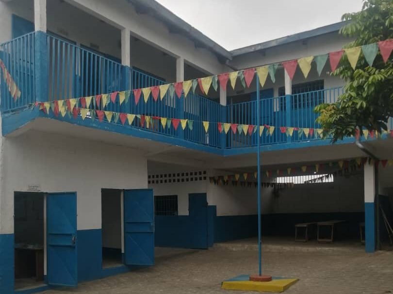 Cour du Site I à Massengo : bâtiment bleu et blanc décoré de fanions